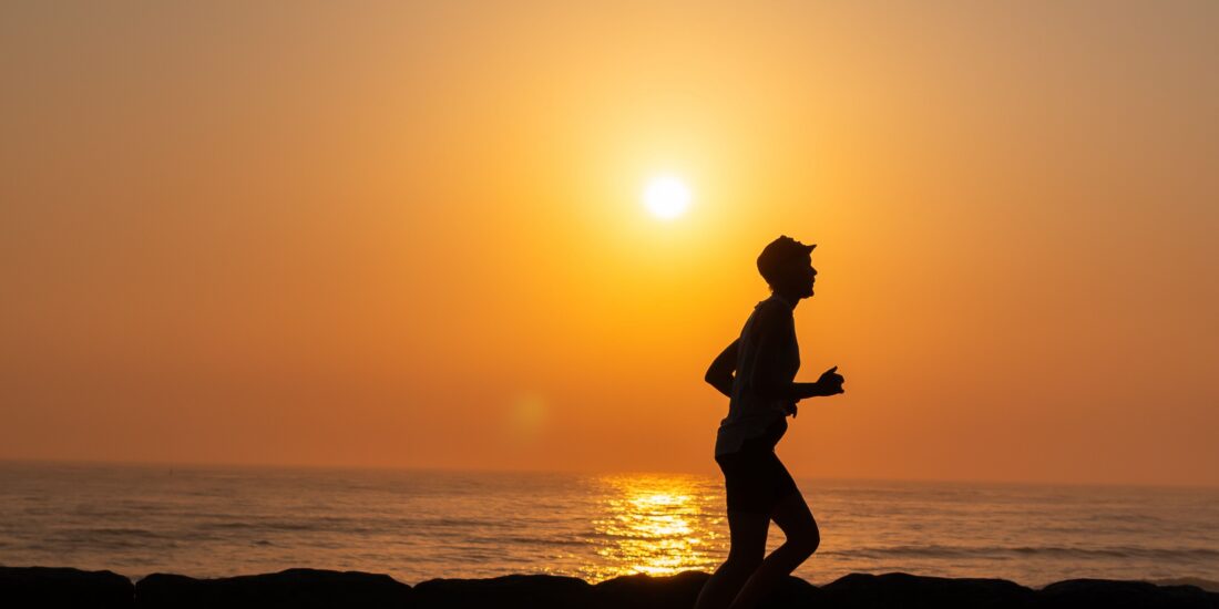 silhouette of a man running on a beach with the sunsetting behind him