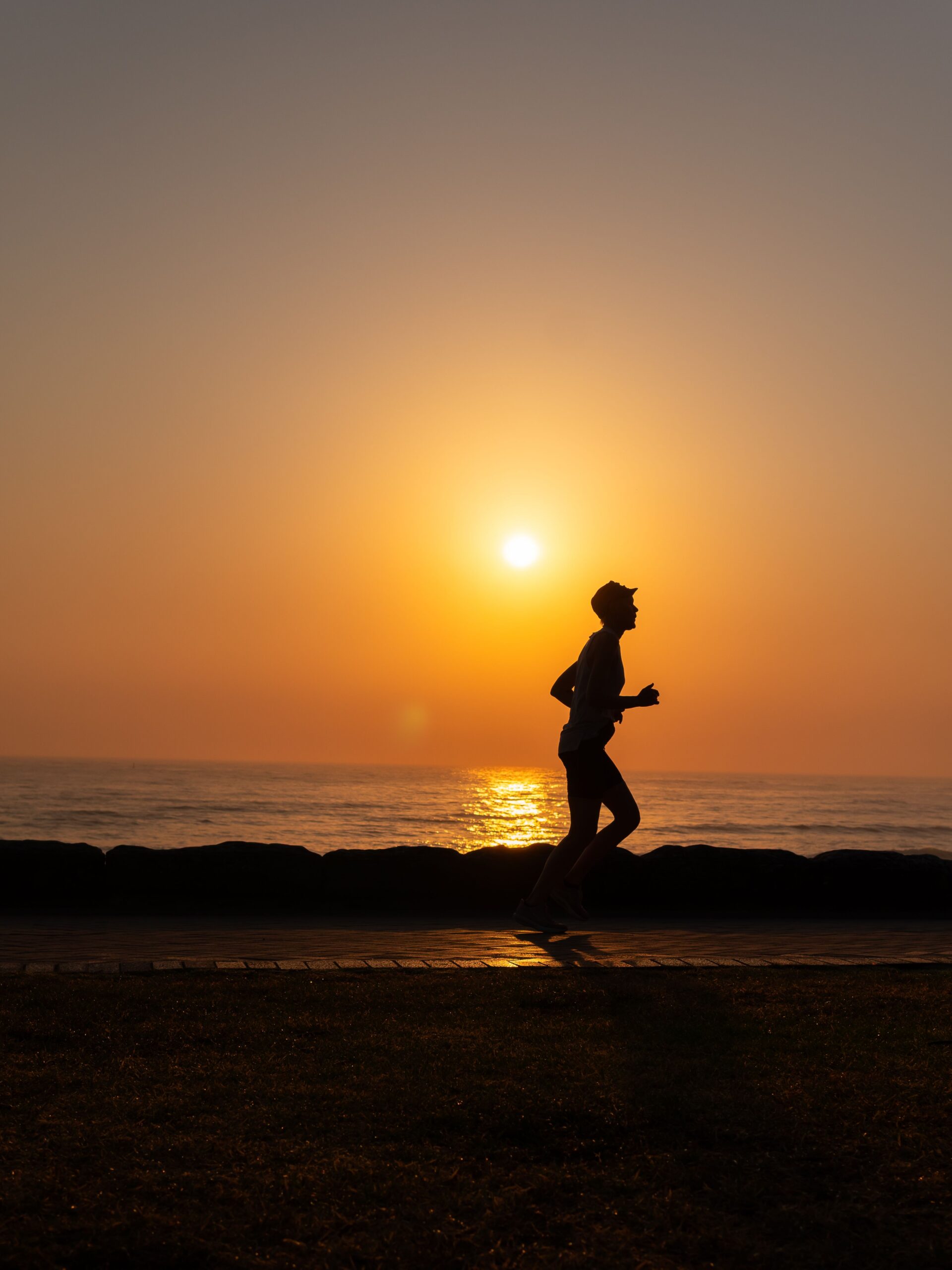 silhouette of a man running on a beach with the sunsetting behind him